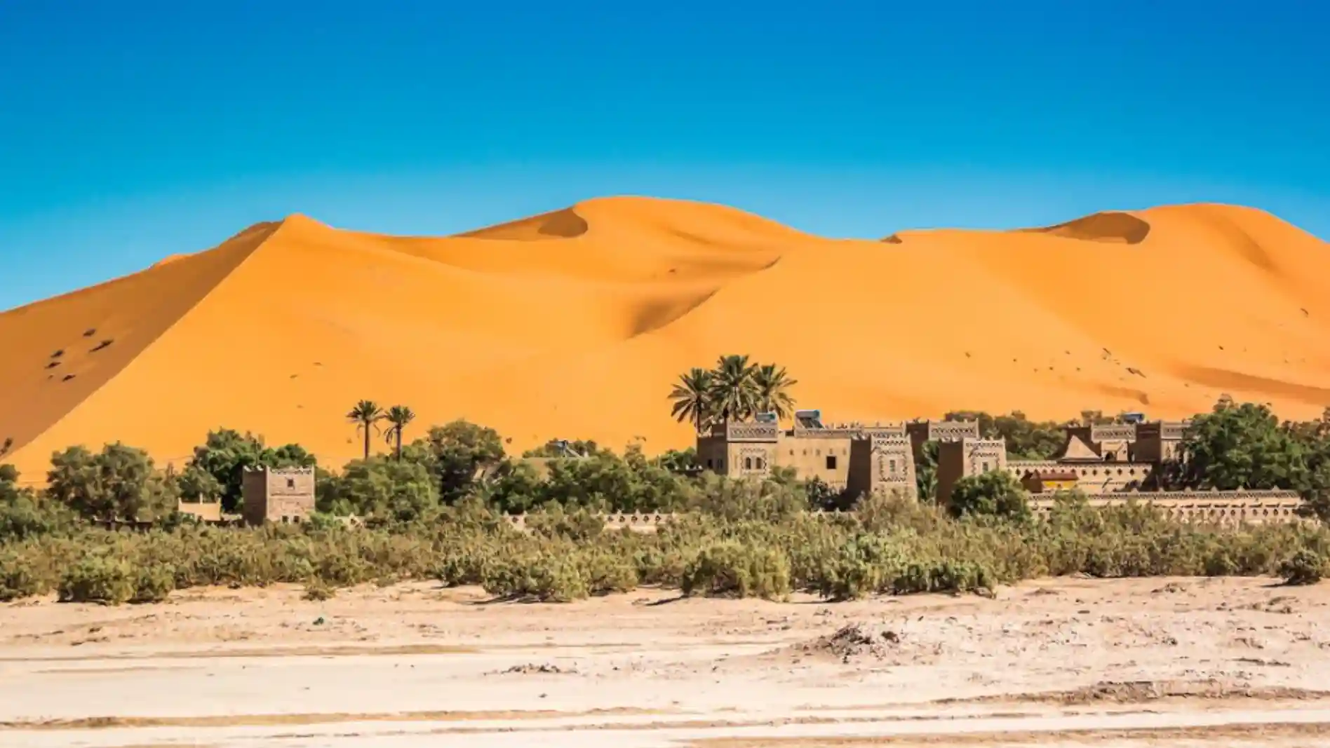 Traditional building complex at the base of the Erg Chebbi dunes in Morocco, surrounded by the vast Sahara Desert landscape.
