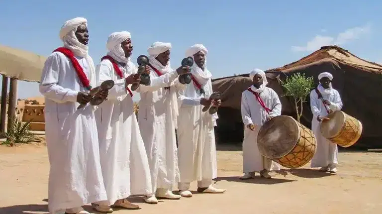 Fes to Marrakech Desert Tour 4 Days 6 Gnawa musicians performing traditional rhythmic music with krakebs during a cultural gathering in Khamlia village, Morocco.