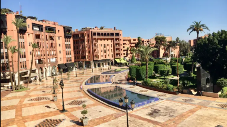 Morocco Itinerary 12 Days 29 Jardin 16 Novembre square in Marrakech’s Gueliz district, featuring a curved fountain, palm trees, and modern urban surroundings.