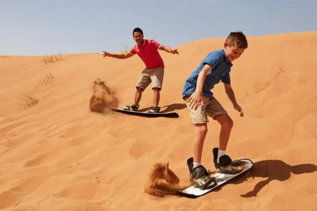 two people sandboarding down a sand dune.