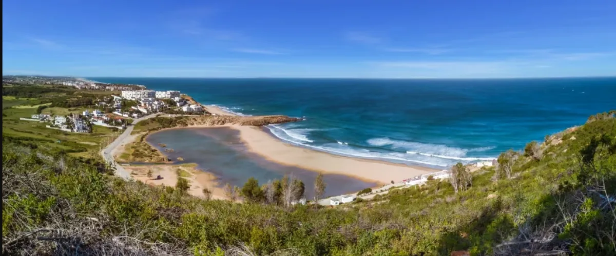 Clean sandy shoreline with dramatic cliffs along the Atlantic coast, featured among the best beaches in Tangier.