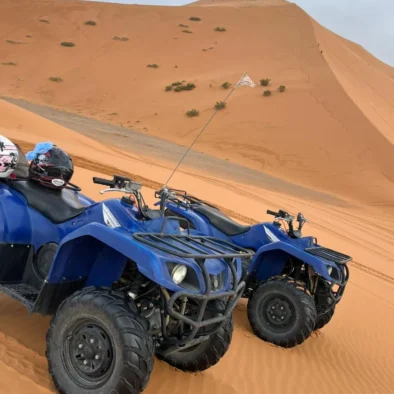 Two blue quad bikes rest on golden desert sand dunes, representing popular recreational activities enjoyed during adventurous desert safari experiences.
