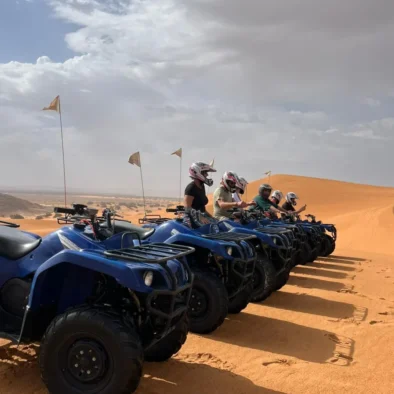 A group pauses during a desert safari adventure on sand dunes, enjoying quad biking amidst the vast and golden desert landscape.