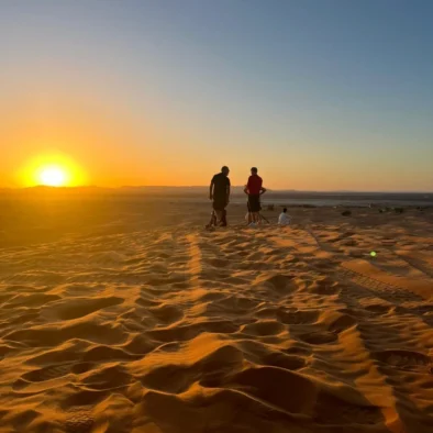 People enjoy a peaceful sunset over rolling sand dunes in Morocco, capturing the serene atmosphere of the desert landscape.